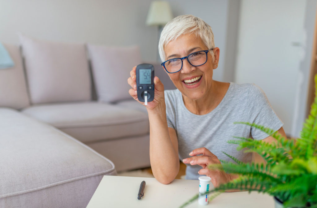 A senior woman smiling and checking her blood sugar level using a glucometer and test strip at home