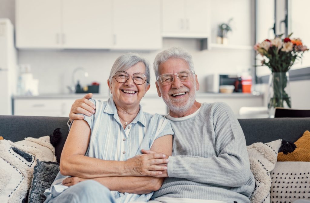 A senior couple smiles as they sit on a couch together in their senior living community